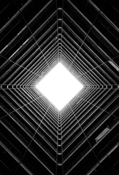 A vertical greyscale low angle shot of the light coming through the ceiling of a tall building